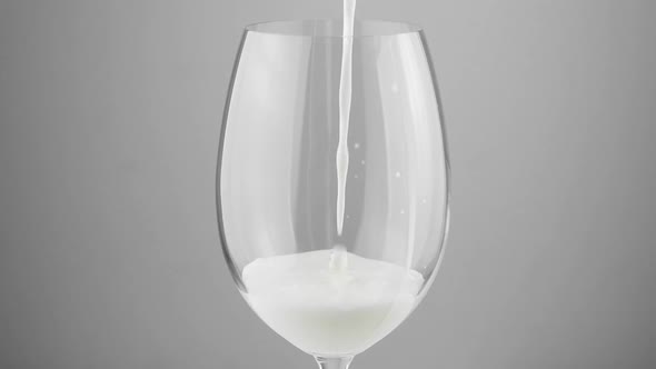 A glass into which white milk is poured on a gray background. Milk in a glass close-up.
