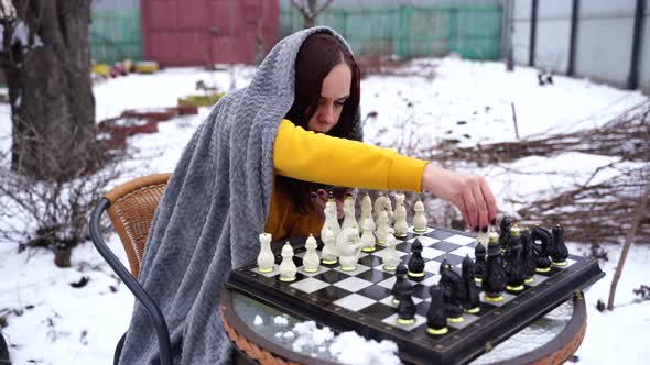 Young Woman Playing Chess and Browsing Smartphone in Yard