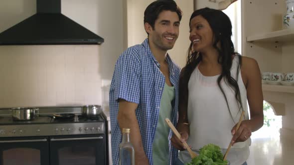 Man kissing a woman while mixing a salad in kitchen