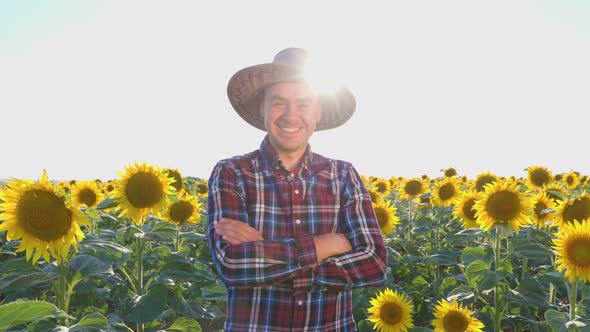 A Happy Young Farmer Stands in a Field with Sunflowers