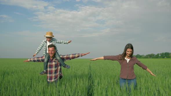 Happy Family in Field, Smiling Male with Child Boy on Shoulders and Female with Arms To Side Walk in