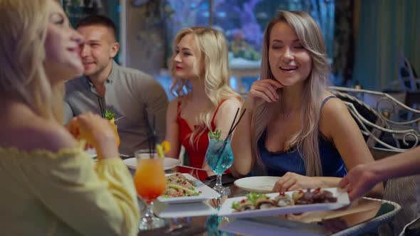 Relaxed Friends Sitting at Table in Luxurious Restaurant As Waiter Bringing Food