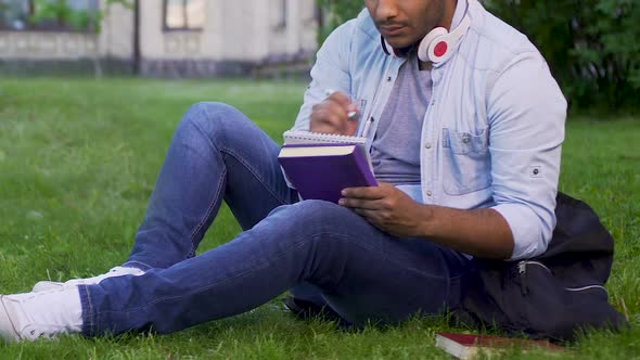 University student sitting on grass, writing essay, literary studies project