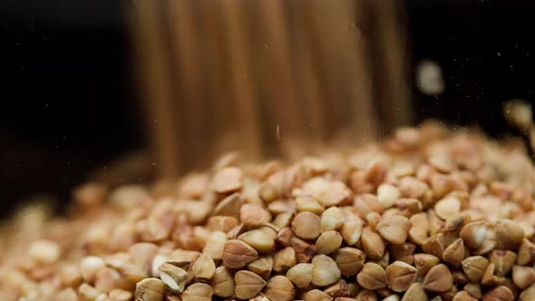 Closeup of Falling Down Buckwheat Into Glass Jar on Black Background