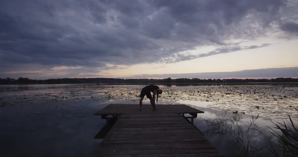 Young Sportsman Doing Muscle Stretching in the Evening in Nature the River Bank