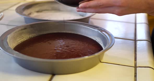 A chef in the kitchen pouring vegan chocolate cake batter into a round baking pan to go in the oven