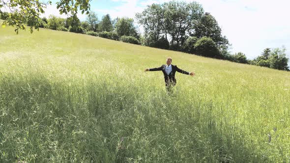 Happy groom running towards his pregnant bride on a summer meadow