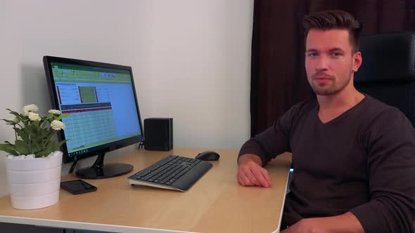 A Young, Handsome Man Sits Next To a Computer and Explains Something To the Camera