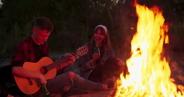 A Young Boy Plays the Guitar While Sitting Around a Campfire with His Friends