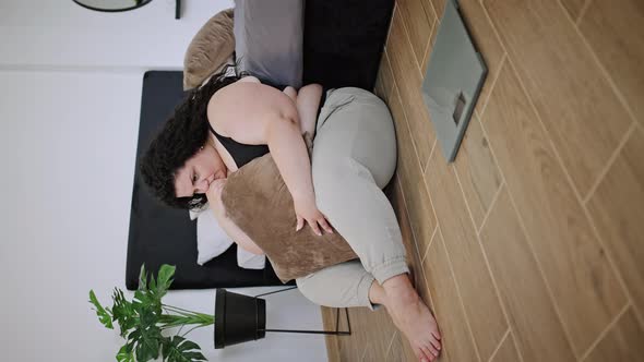 Overweight Woman Sits and Hugs Pillow Looking at Scales