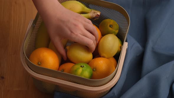 A woman putting her hand into a basket of fruit and pulling out a lemon