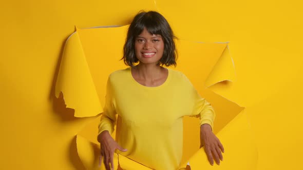 Young Woman Makes Winning Gesture Exclaims Yes Through Hole of Yellow Background