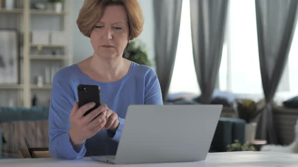 Old Senior Woman Using Smartphone and Laptop at Workplace