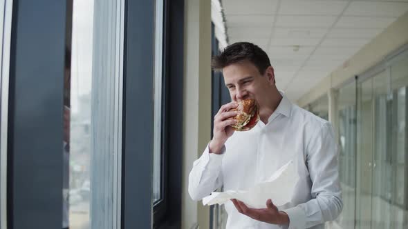 Young Office Manager in Shirt Eating Tasty Hamburger, Having Pleasure Indoors