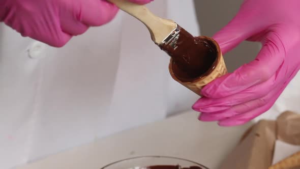 A Woman Smears Waffle Cones With Liquid Chocolate. Makes Horns With Chocolate And Marshmallows