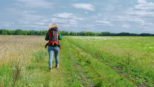 A Young Woman is Walking Along a Cereal Field