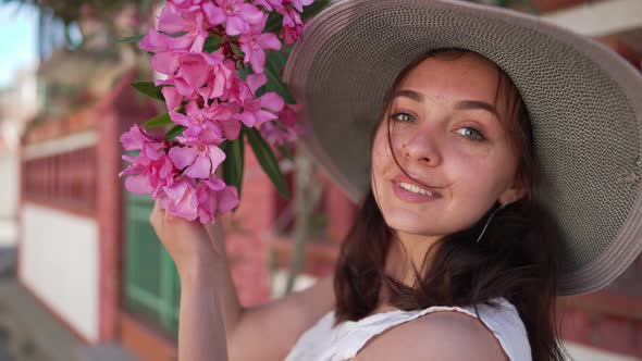 Closeup Portrait of Young Gorgeous Woman Admiring Pink Flowers on Tree Branch and Looking at Camera