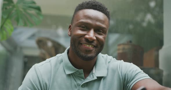 Portrait of happy african american man sitting and looking at camera in garden