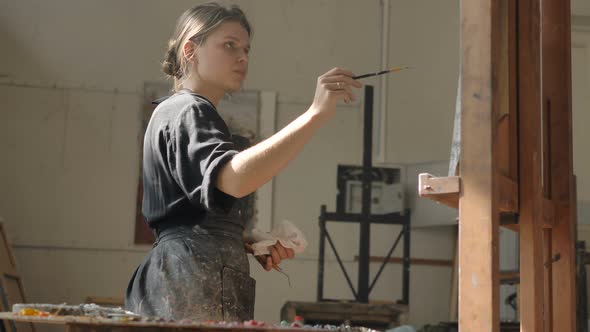 Woman in Dirty Apron Draws Picture on Canvas Put on Easel