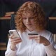 Pretty Redhaired Woman is Making Online Payment Holding Bank Credit Card Using Smartphone at Office - VideoHive Item for Sale