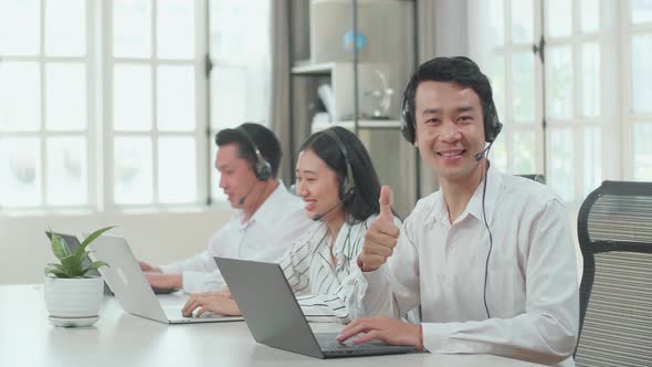 A Man Of Three Asian Call Centre Agents Wearing Headset And Smile To Camera Then Thumbs Up