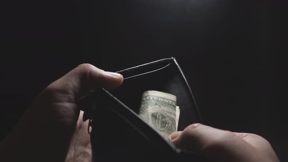 Man's Hand Takes the Last Dollar Out of His Wallet, a Close-up of the Hand on a Dark Background, One