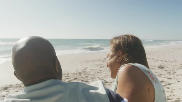 Smiling senior african american couple embracing and looking at sea on sunny beach