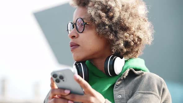 Serious adult African woman wearing casual clothes texting by phone and looking around