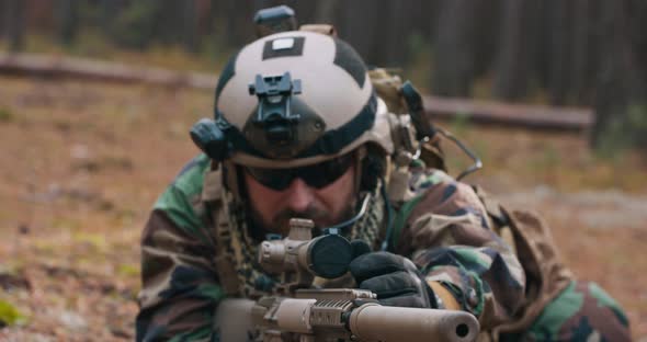 A Bearded Soldier is Put on the Forest Litter in a Tactical Military Uniform with a Helmet on His