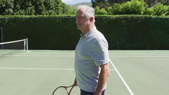 Portrait of smiling senior caucasian man holding tennis racquet on tennis court on sunny day