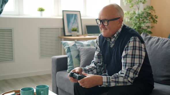 Joyful Senior Man Playing Video Game Alone Entertaining at Home Enjoying Gaming