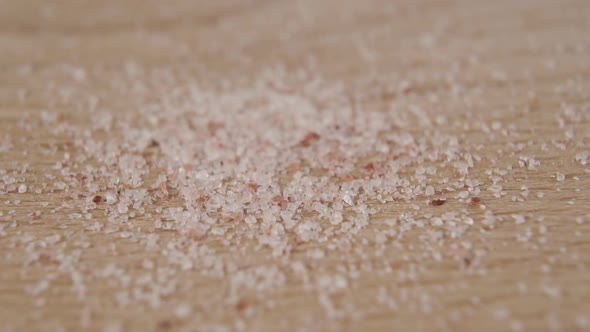 Crumbs of powdered Himalayan pink salt are poured onto a wooden cutting board in slow motion