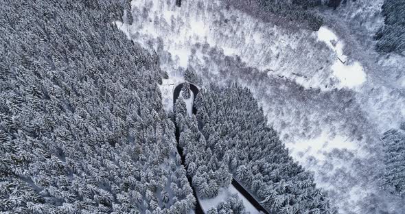 Forward Aerial Top View Over Hairpin Bend Turn Road in Mountain Snow Covered Winter Forest