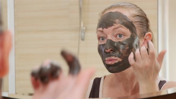 Portrait of adult woman applying black rejuvenating mask to face