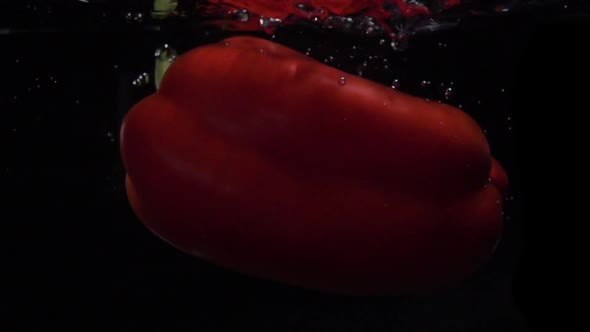 Red Bell Pepper Falls Into Water. Slow Motion. Black Background. Food Video