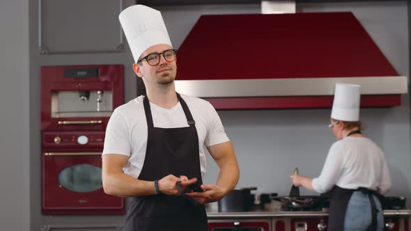 Portrait of Young Chef of Big Restaurant Tying Apron and Smiling in Modern Kitchen