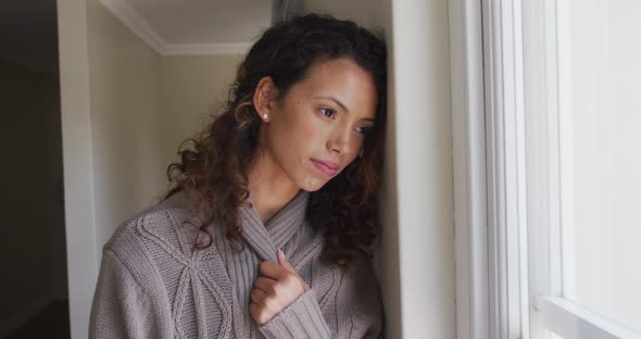 Thoughtful biracial woman standing at window and looking into distance