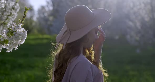 Girl with Long Light Brown Hair Grey Eyes Wearing Pink Dress and Hat Walks Through Apple Gardens