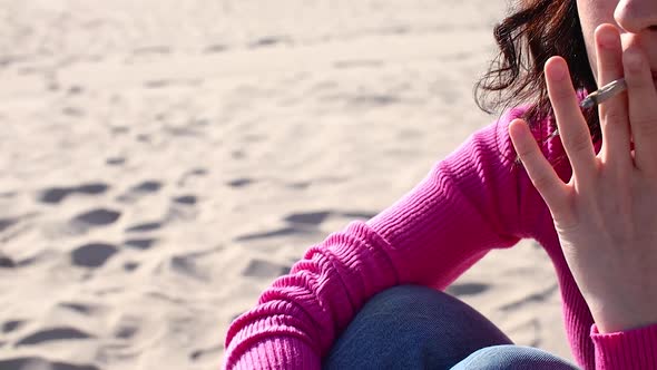 Young Woman Smokes a Cigarette on the Sand