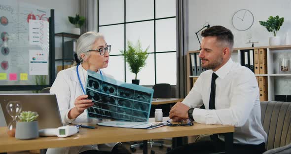 Female Radiologist in Glasses Having Conversation with His Male Handsome Patient while Holding xray