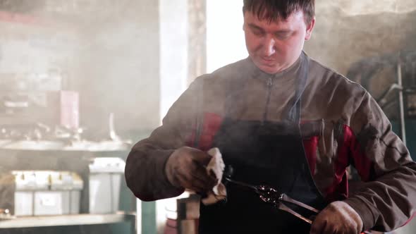 The Blacksmith Holds the Cooled Metal Detail with Tongs and Wipes It with a Rag