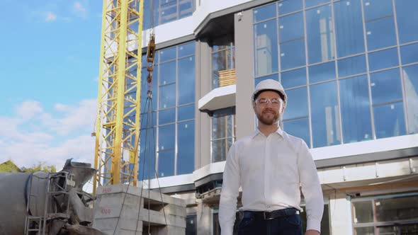 An Engineer in a White Shirt and Helmet Stands Against the Backdrop of a Modern Glass Building