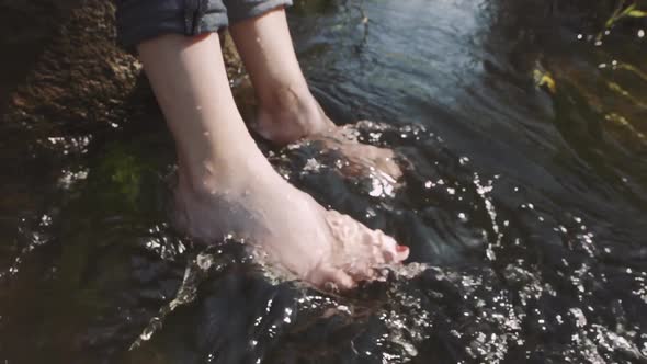 Woman Relaxes By River Sitting on Edge of Rock Swing One's Feet on Water Flow