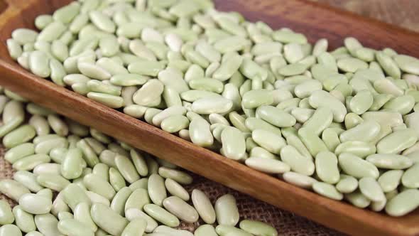 Dry green Verdina beans falling into wooden ware close up. Uncooked legumes