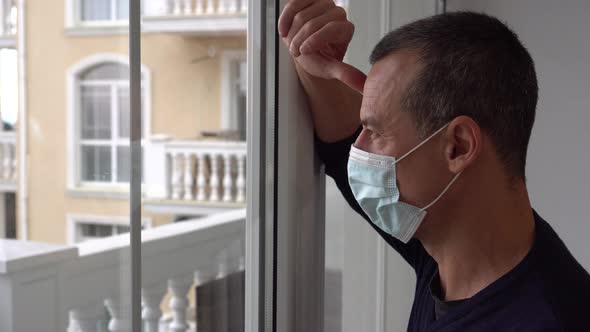 Lockdown COVID-19. Man in protective medical masks sad looks at the city through the window