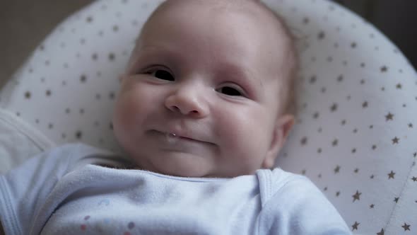 Portrait Of CloseUp Face Of Smiling Newborn Baby Lying In Toddler Crib