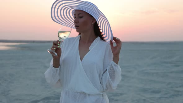 Elegant Woman with Glass of Wine Resting on Beach at Sunset