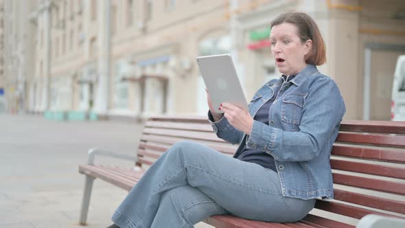 Old Woman Reacting to Loss on Tablet While Sitting Outdoor on Bench