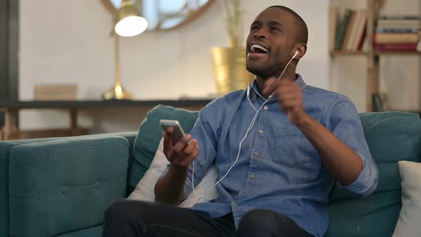 Young African Man Listening Music on Smartphone on Sofa