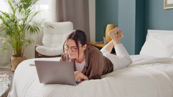 Young woman on the bed typing and working on a laptop, distance learning. Freelancer, distant job